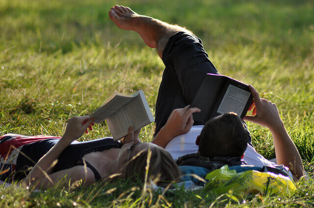 two people reading books at park - Paperback Book vs. Kindle eBook Readers