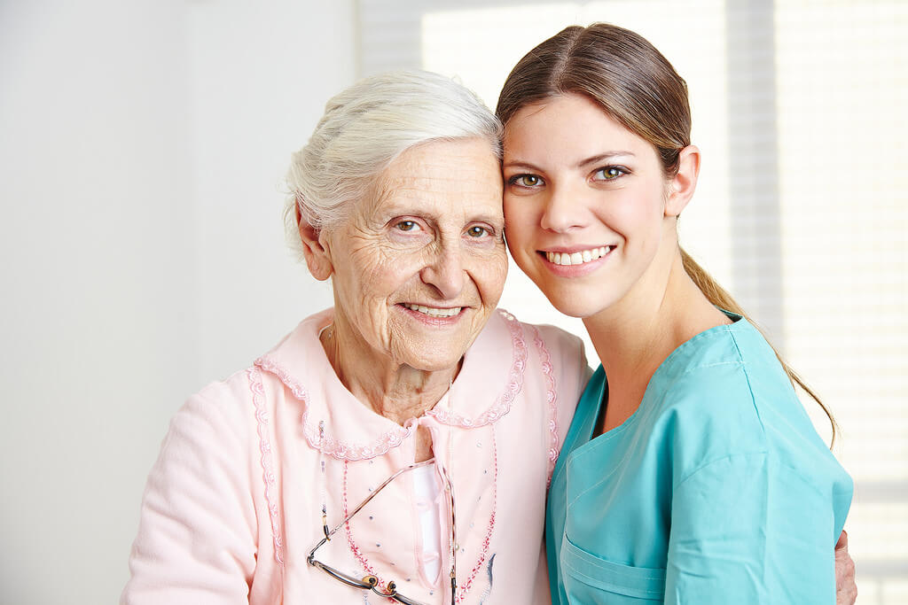 Smiling caregiver caregiving happy senior woman in nursing home