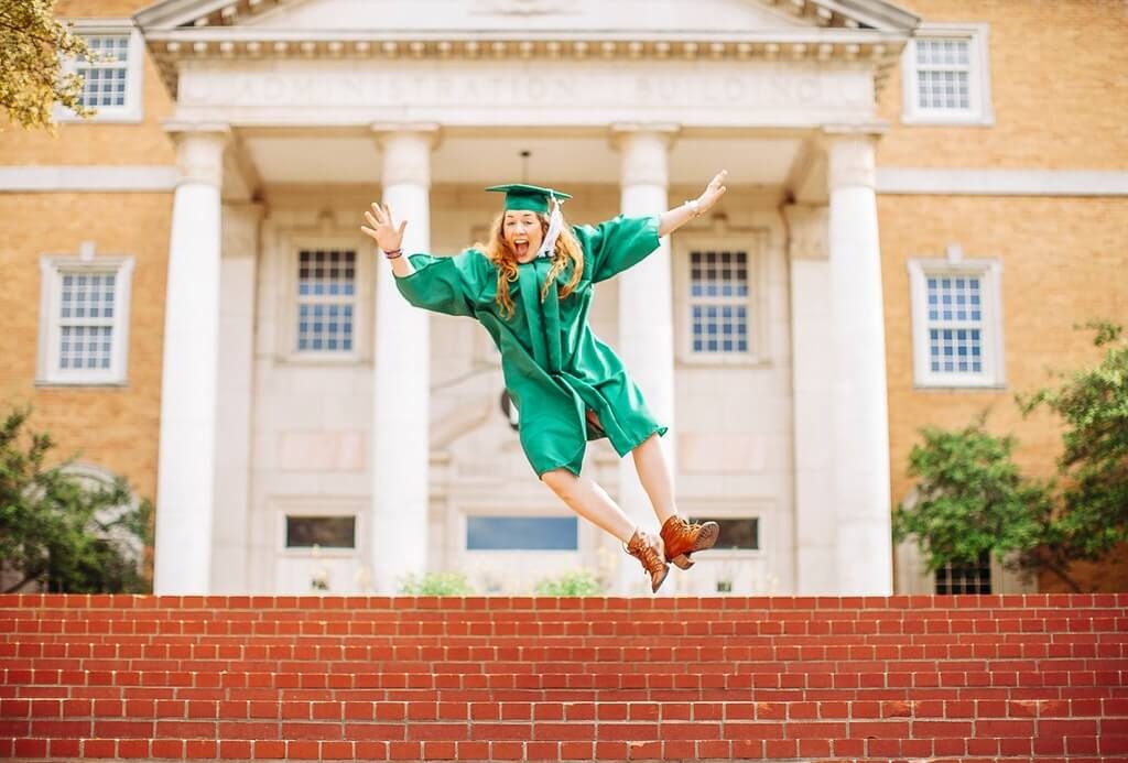 Woman jumping above stairs wearing graduation gown and a hat.