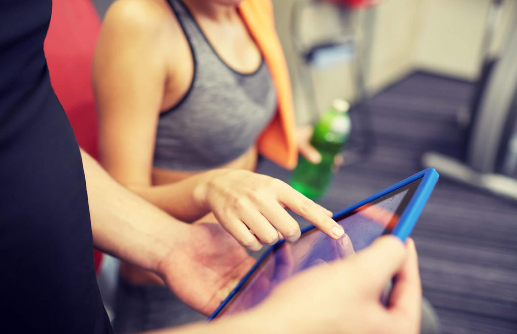 Personal Trainer and Gym Software. Close up of trainer hands with tablet PC in gym.