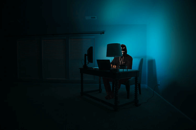 A man at a computer disguised as an anonymous hacker wearing a Guy Fawkes mask