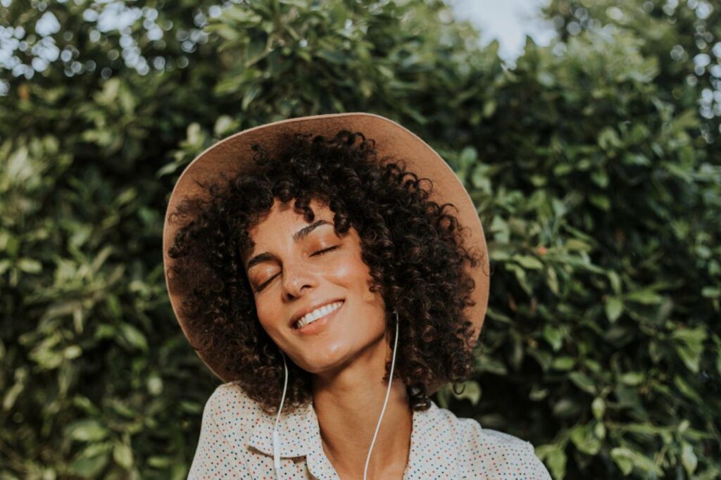 smiling woman listening to music in a botanical garden, emotional resilience, positive mood