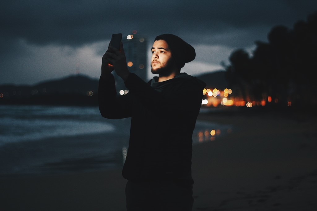 Man capturing Milky Way using smartphone on beach during dusk photo