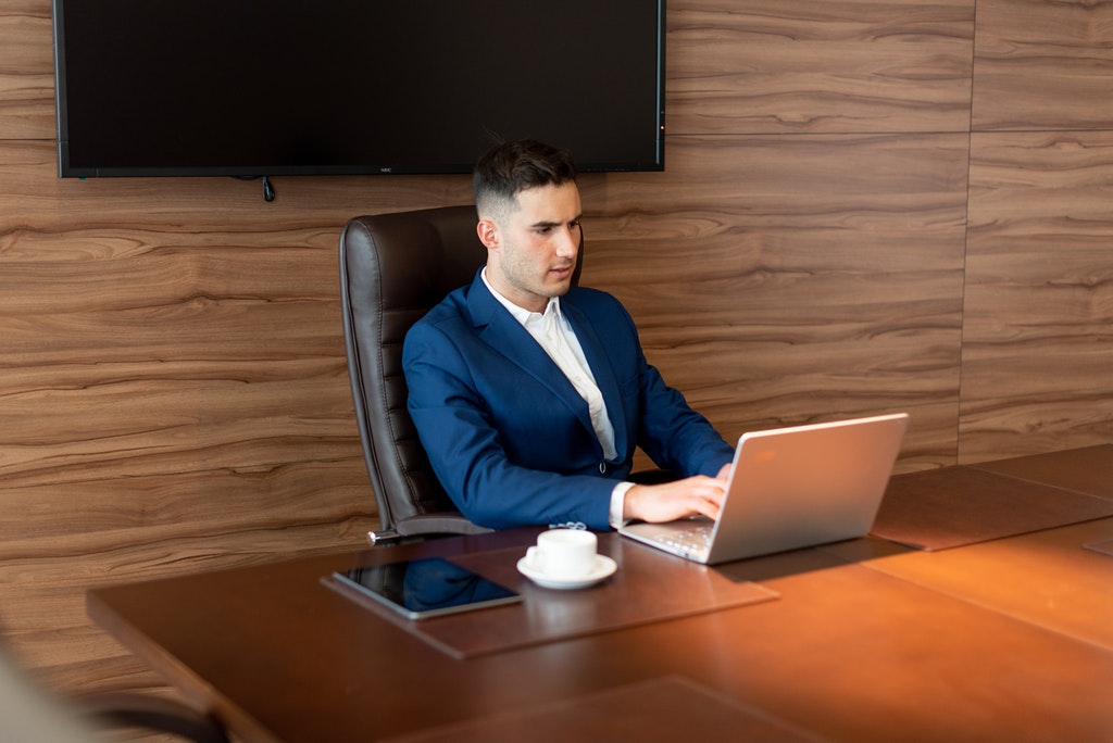 Man in Blue Suit Sitting at His Desk Using Laptop