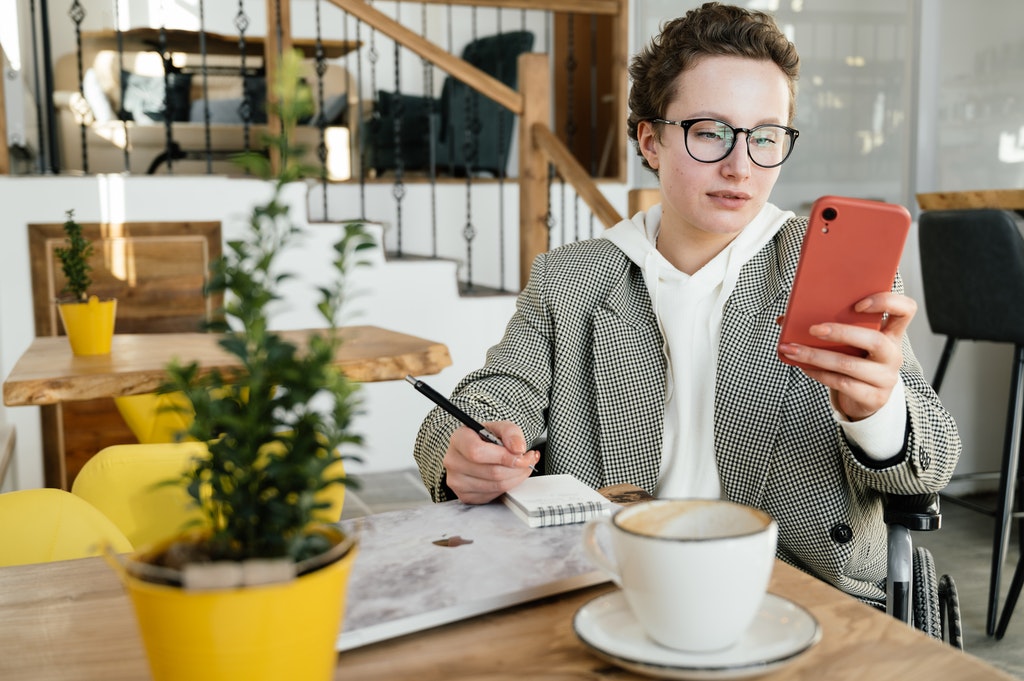 Woman Creating Event Budget Holding Smartphone Writing on Notebook