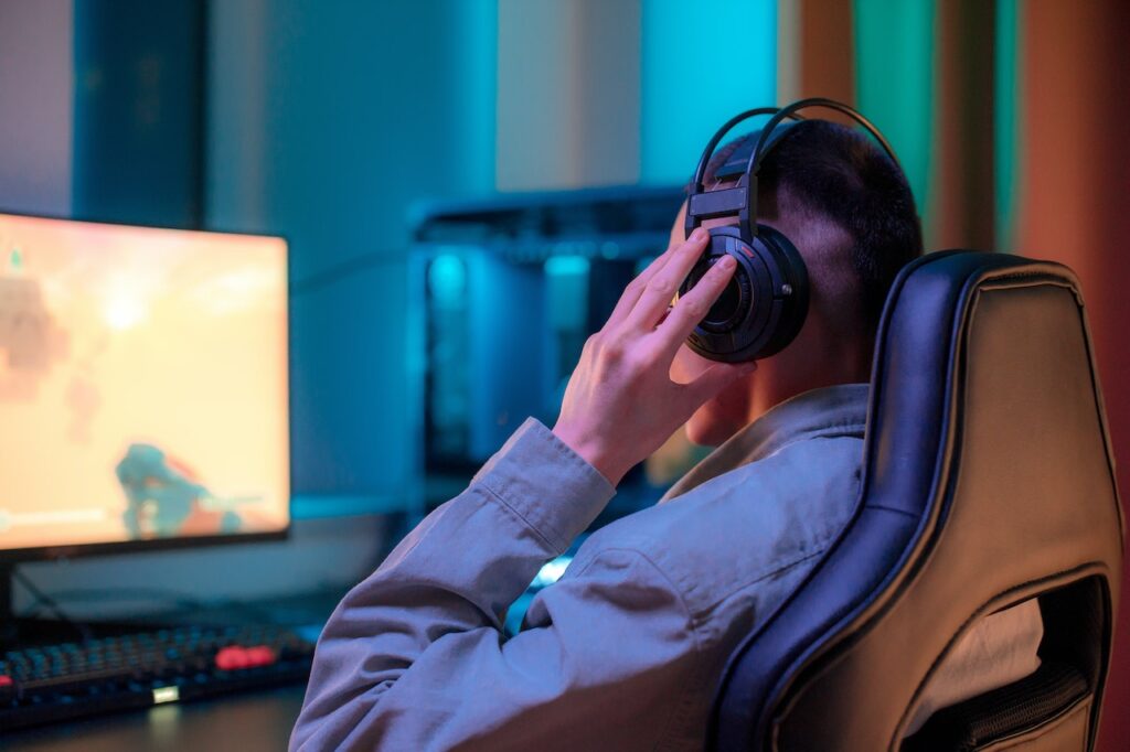 Man Holding His Gaming Headset While Playing on a Computer
