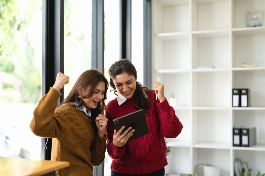 Two successful business women arms up celebrating with tablet computer
