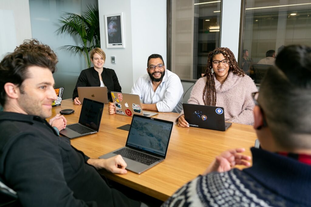 Team meeting where employees are smiling and sitting at a desk discussing proposal management software