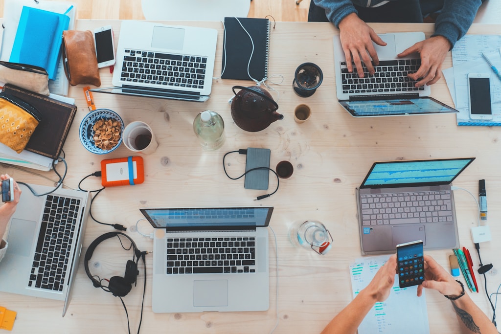 Tech Team People Sitting Down Near Table With Assorted Laptop Computers